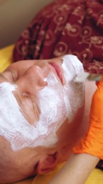 Kozmetoloji, yüz bakımı prosedürleri. Yakın plan. Bir kadının yüzünde altın aljinat kozmetik maske kullanma prosedürü. Yaşlanma karşıtı kozmetikler.