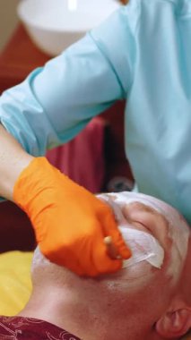 Kozmetoloji, yüz bakımı prosedürleri. Yakın plan. Bir kadının yüzünde altın aljinat kozmetik maske kullanma prosedürü. Yaşlanma karşıtı kozmetikler.