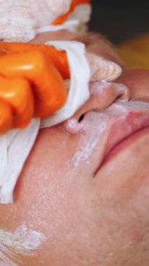 Kozmetoloji, yüz bakımı prosedürleri. Yakın plan. Bir kadının yüzünde altın aljinat kozmetik maske kullanma prosedürü. Yaşlanma karşıtı kozmetikler.