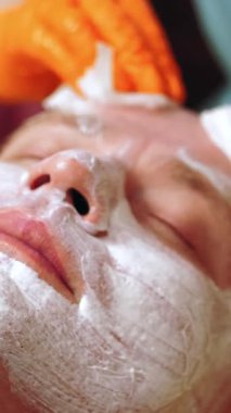 Kozmetoloji, yüz bakımı prosedürleri. Yakın plan. Bir kadının yüzünde altın aljinat kozmetik maske kullanma prosedürü. Yaşlanma karşıtı kozmetikler.