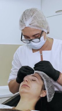 Güzellik iğnesi. Yaşlanma önleyici iğneler. Botulinum terapisi. Yüz tazeleme. Doktor, güzellik enjeksiyonlarından önce hastanın alnını antiseptik pamukla siliyor. Güzellik konsepti.