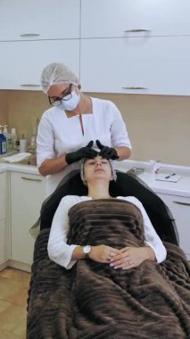 Yaşlanma karşıtı kozmetoloji. Yüz masajı. Kadın yüz masajı yaptırıyor. Güzellik kliniğinde kasları ve yüz derisini yumuşattığı için lenfatik drenaj yaptırıyor. Cilt bakımı, kadınlar için kozmetik prosedürleri.