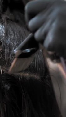 Saç boyama. Saç boyası. Yakın plan. Renkçi usta, kuaförde ya da kuaförde kadın esmer saç köklerine saç fırçasıyla saç boyası uyguluyor..