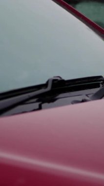 Şiddetli yağmur, duş, damlalar arabanın kaputuna düşer. Boş kırmızı araba silecekleri park yerinde durur. Damlacıklar küçük akarsularda akıyor