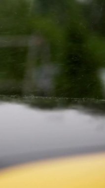 Sağanak yağmur, sağanak yağmur, damlalar yağmur damlacıklarıyla birlikte, park yerinde duran siyah ve sarı kaputun ıslak yüzeyine düşüyor. Araba yağmurda ıslanır.