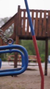 Çocuk parkına yağmur yağıyor. Yakın plan. Boş ıslak salıncak rüzgarda sallanıyor, boş oyun parkında, bahçede, sağanak yağmur altında.