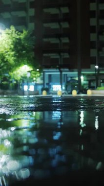 Hafif yağmur. Şehir kaldırımında ışık yansıyan su birikintisi. Sokak lambası. Sokak Işıklarıyla Yağmur Damlası.