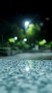 Gece yağmur yağacak. Su birikintisi Sokak lambası. Su birikintisine düşen yağmur damlaları. Yakın plan..