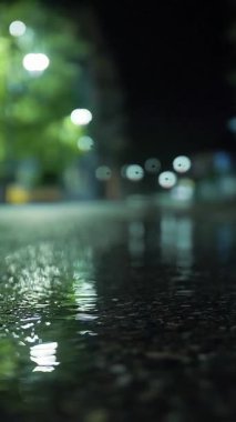 Gece yağmur yağacak. Su birikintisi Sokak lambası. Su birikintisine düşen yağmur damlaları. Yakın plan..