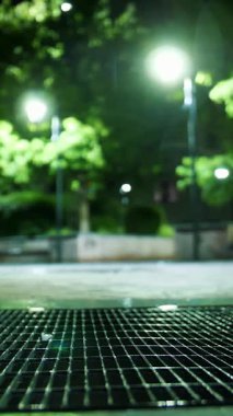 Fırtına kanalizasyonu. Hafif yağmur. Şehir kaldırımında ışık yansıyan su birikintisi. Sokak lambası. Sokak Işıklarıyla Yağmur Damlası.