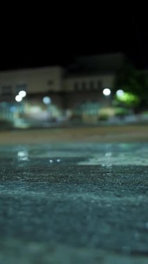 Hafif yağmur. Şehir kaldırımında ışık yansıyan su birikintisi. Sokak lambası. Sokak ışıklarıyla yağmur damlası. Yakın plan..