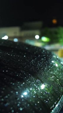 Gece yağmur yağacak. Yağmur damlaları içinde araba kaputu. Su birikintisi Sokak lambası. Su birikintisine düşen yağmur damlaları.