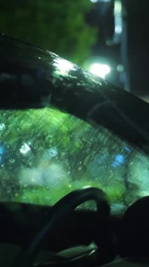 Yağmur damlalarında araba camı. Hafif yağmur. Şehir kaldırımında ışık yansıyan su birikintisi. Sokak lambası. Sokak ışıklarıyla yağmur damlası. Yakın plan..