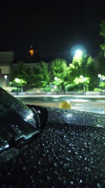 Yağmur damlaları içinde araba kaputu. Yağmur. Su birikintisi. Geceleri şehir. Sokak ışıklarıyla yağmur damlası. Yakın plan..