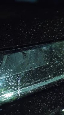 Yağmur damlalarında araba farları. Hafif yağmur. Şehir kaldırımında ışık yansıyan su birikintisi. Sokak lambası. Sokak ışıklarıyla yağmur damlası. Yakın plan..