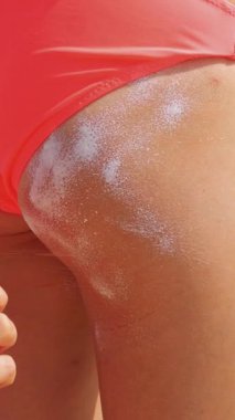 Yakın çekim, güneş kremi sürme ya da kalça derisine sprey sürme. Sahilde, güneşin altında, denizin arka planında. Güneş ve ultraviyole koruma. cilt koruması