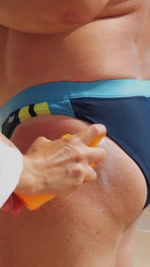 Yakın çekim, güneş kremi sürme ya da erkek derisine sprey sürme. Sahilde, güneşin altında, denizin arka planında. Güneş ve ultraviyole koruma. cilt koruması