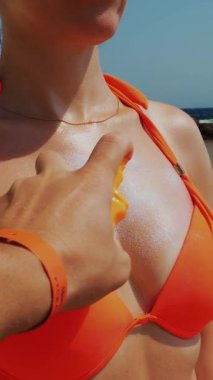 Erkek eli yakın plan güneş kremi sürüyor ya da kadın dekolte cildine sprey sürüyor. Sahilde, güneşin altında, denizin arka planında. Güneş ve ultraviyole koruma. cilt koruması