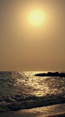 Güneş doğarken ya da batarken deniz manzarası. Küçük dalgalar, kayalık kıyılar, güneş ışınları suya yansıyor..