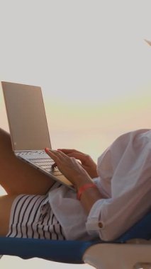 Güneş gözlüklü ve güneş şapkalı genç bir kadın, dizüstü bilgisayar kullanıyor, gün batımında ya da gün doğumunda, havuzda uzanıyor. Serbest çalışan, uzaktan kumandalı. Yaz tatili tatil beldesinde.