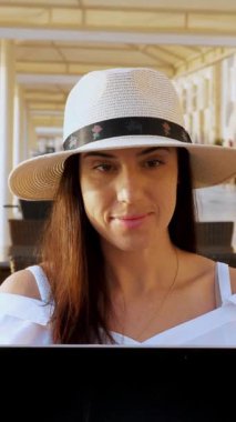 Yaz kıyafetleri ve güneş şapkası takan genç bir kadın dizüstü bilgisayar kullanıyor. Gün batımında ya da gün doğumunda deniz kenarında tek başına oturuyor. Serbest çalışan, uzaktan kumandalı. Denizde yaz tatili