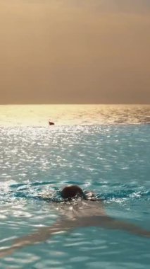 İnsanlar güneş doğarken panoramik deniz manzaralı sonsuz havuzda yüzerler. seyahat ve tatil kavramı