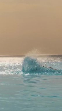 Adam ustalıkla yüzüyor, bir vuruşla, güneş doğarken, panoramik deniz manzaralı sonsuz havuzda tekniğini geliştiriyor. spor, seyahat ve tatil konsepti