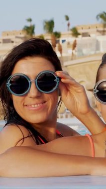 Kadın ve genç kız, anne ve kız, komik, tıpatıp aynı, yuvarlak güneş gözlükleriyle, rahatlayın, lüks otel manzaralı açık havuzda eğlenin. Aile tatili kavramı