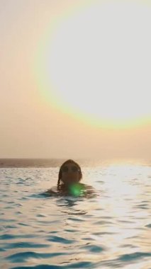 Siluet, güneş gözlüklü kadın güneş doğarken panoramik deniz manzaralı sonsuz havuzda yüzer. seyahat ve tatil kavramı
