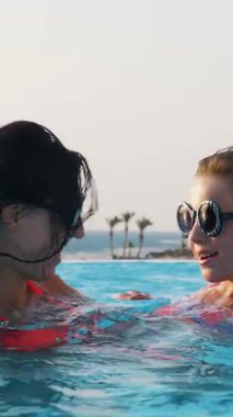 Kadın ve genç kız, anne ve kız, komik, tıpatıp aynı, yuvarlak güneş gözlükleriyle, rahatlayın, lüks otel manzaralı açık havuzda eğlenin. Aile tatili kavramı