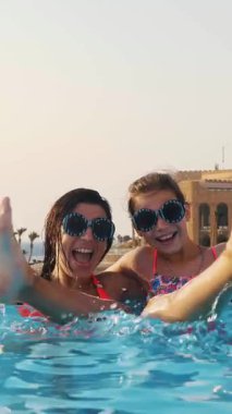 Kadın ve genç kız, anne ve kız, komik, tıpatıp aynı, yuvarlak güneş gözlükleriyle, rahatlayın, lüks otel manzaralı açık havuzda eğlenin. Aile tatili kavramı