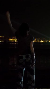 Gece, bir kadın dans ediyor, arkadan manzara. suyun üzerinde parlayan şehrin ışıklarına karşı