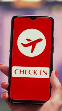 Uçak simgesi, giriş işareti olan akıllı telefonu havaalanının kalkış terminalinde, uçuş bilgi panosunun önünde, ekranda tutarken..