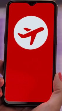 Uçak ikonlu akıllı telefonun yakın plan çekimi, tatil tabelası yok, ekranda, kalkış terminalinde, havaalanındaki uçuş bilgi panosunun önünde..