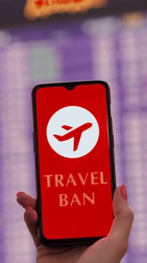 Yaklaş, kadın, koruyucu maskeli, akıllı telefonu uçak ikonu, seyahat yasağı tabelası, ekranda, kalkış terminalinde, havaalanında uçuş bilgi panosunun önünde tutuyor..