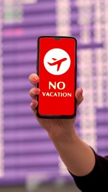 Yaklaş, kadın, koruyucu maskeli, uçak ikonlu akıllı telefonu tutuyor, tatil tabelası yok, ekranda, kalkış terminalinde, havaalanında, uçuş bilgi panosunun önünde.