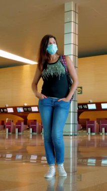 Kadın gezgin, koruyucu maskeli, boş bir havaalanında. Kapalı gişelerin arka planı. Coronavirus salgını sırasında seyahat etmek ya da tecrit