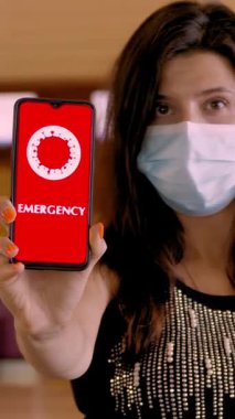 Kadın, koruyucu maskeli, elinde COVID-19 simgesiyle akıllı telefon tutuyor, mesaj - acil, ekranda, havaalanındaki boş kayıt gişelerinin önünde