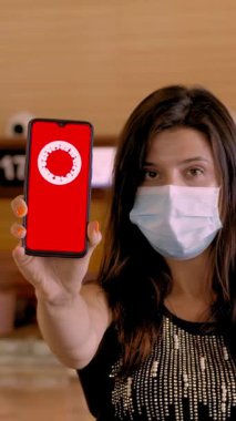 Kadın, koruyucu maskeli, elinde COVID-19 simgesi, mesajı olan akıllı telefonu var. Seyahat yasağı, ekranda, havaalanındaki boş kayıt gişelerinin önünde..