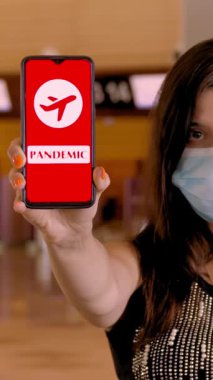 Koruyucu maskeli bir kadın, elinde uçak ikonu, mesaj, salgın hastalığı olan akıllı telefonu havaalanındaki boş gişelerin önünde tutuyor..