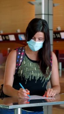Koruyucu maskeli bir kadın, evrakları dolduruyor, havaalanında tıbbi anket dolduruyor. Coronavirüs salgınından sonra yeni kurallar ve kısıtlamalar. Uçuşların devamı, açık sınırlar
