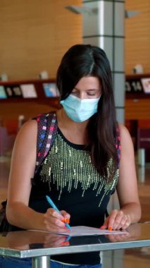 Koruyucu maskeli bir kadın, evrakları dolduruyor, havaalanında tıbbi anket dolduruyor. Coronavirüs salgınından sonra yeni kurallar ve kısıtlamalar. Uçuşların devamı, açık sınırlar