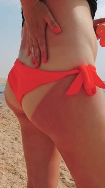 Güneş yanığı. Yakın plan. Genç bir kadın güneş kremi sürüyor ya da ciddi şekilde yanmış, kıça kırmızı bir cilt kremi sürüyor, plajda, deniz kenarında, sıcak ve güneşli bir günde. cilt UV koruması.