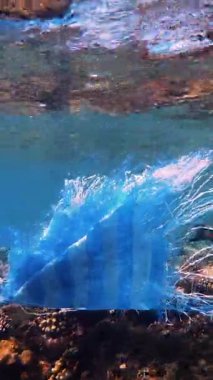 Denizde çöp. Denizin plastik kirliliği. Mavi plastik poşet güneş ışığında yavaşça suyun altında sürükleniyordu. Arka ışıklandırma. Plastik atık çevresel kirlilik sorunu