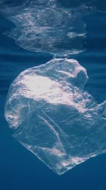 Denizde çöp. Denizin plastik kirliliği. Kullanılmış, şeffaf plastik torba güneş ışığında yavaşça suyun altında sürükleniyor. Arka ışıklandırma. Plastik atık çevresel kirlilik sorunu
