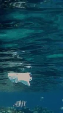 Denizde çöp. Denizde tıbbi maske. Tıbbi maskeler güneş ışığında yavaşça suyun altında sürükleniyorlar. Arka ışıklandırma. Çöp çevresi kirliliği sorunu