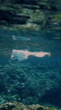 Denizde çöp. Denizde tıbbi maske. Tıbbi maskeler güneş ışığında yavaşça suyun altında sürükleniyorlar. Arka ışıklandırma. Çöp çevresi kirliliği sorunu