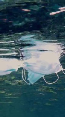 Denizde çöp. Denizde tıbbi maske. Tıbbi maskeler güneş ışığında yavaşça suyun altında sürükleniyorlar. Arka ışıklandırma. Çöp çevresi kirliliği sorunu