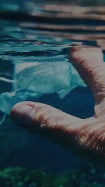 Denizde çöp. Denizi temizle. Denizde tıbbi maske. Sudaki çöpleri toplayın. Yakın plan. Erkek el atıkları yakalar, tıbbi maske kullanır. Birinci şahıs görüşü. Deniz ya da okyanus kirliliği. çevre koruması.