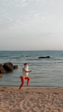 Komik Noel Baba. Deniz kenarındaki Noel Baba. Noel Baba acele ediyor. Tişörtlü ve kırmızı taytlı Noel Baba deniz kıyısında koşar. sıcak yaz günü.